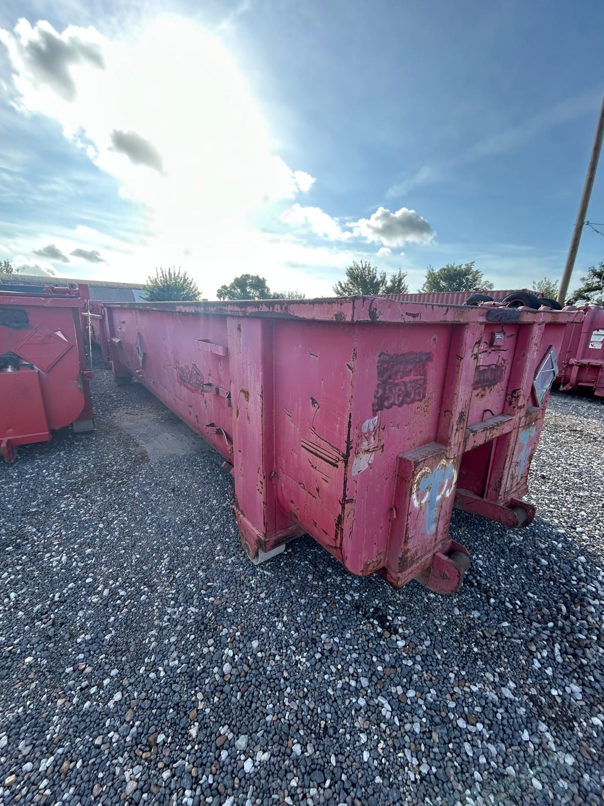 Used red open top roll-off container in a gravel yard