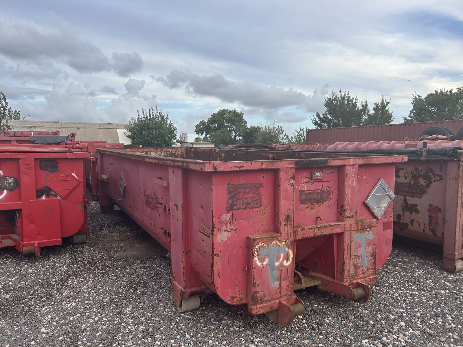 Used red open top roll-off container in a gravel yard